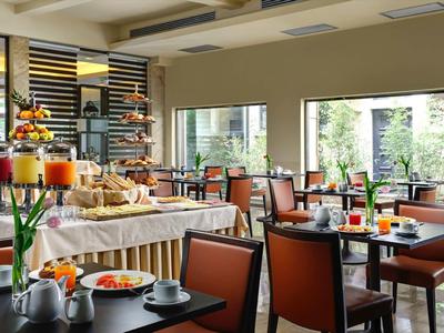 Hell eingerichteter Frühstücksraum mit Sitzgruppen, Buffet und großen Fenstern zum Außenbereich.