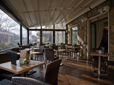 Helles, gemütliches Café mit Holzboden, modernen Tischen und Stühlen, Pflanzen und großen Fenstern.