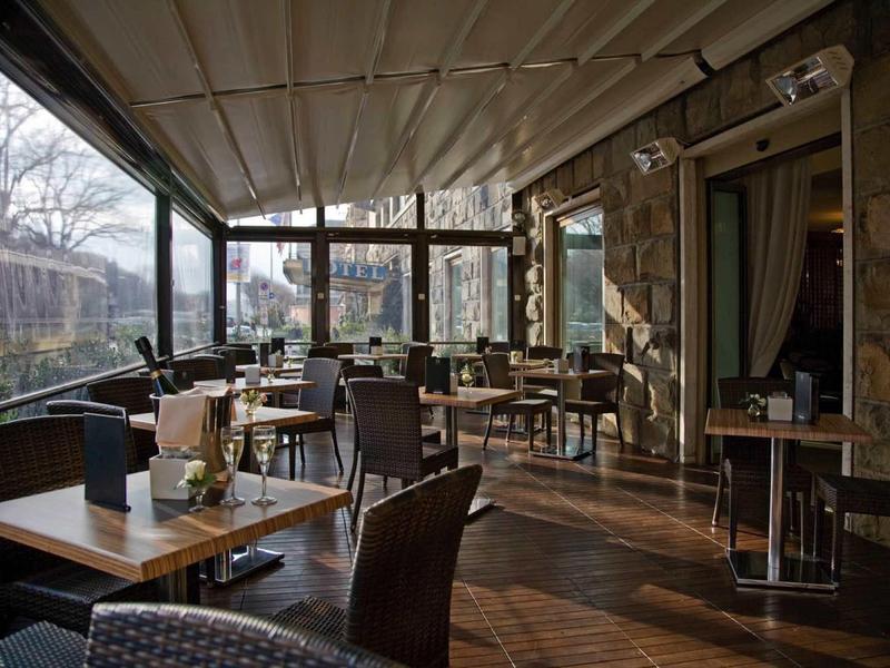 Helles, gemütliches Café mit Holzboden, modernen Tischen und Stühlen, Pflanzen und großen Fenstern.