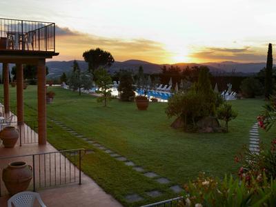 Vista su un giardino con piscina al tramonto, terrazza con tavoli e sedie a sinistra.