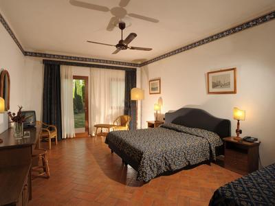 Pohodlný hotelový pokoj s manželskou postelí, psacím stolem a balkonem s výhledem do zahrady.