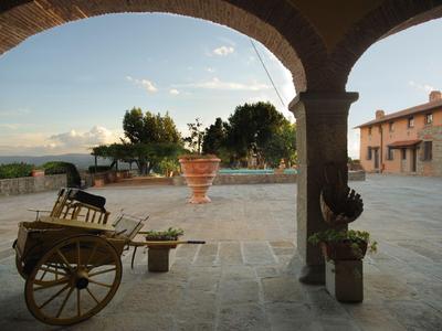 Veduta di un cortile di pietra con vecchi edifici, piante e un carretto sotto un arco