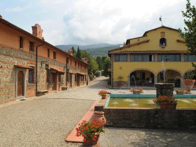 Cortile con sentiero, due edifici in pietra e intonaco giallo e una piccola fontana.