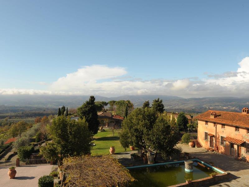 Krajina s stromy, budovami a horami pod modrou oblohou.