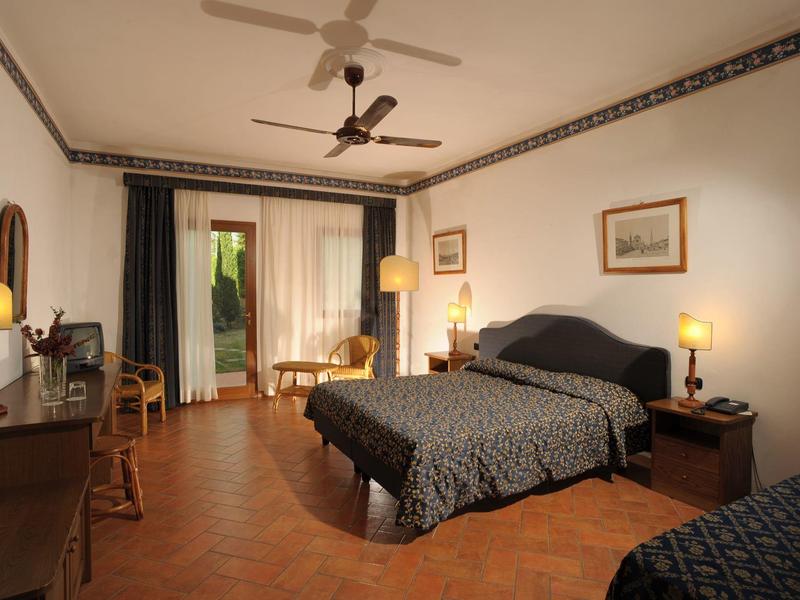 Pohodlný hotelový pokoj s manželskou postelí, psacím stolem a balkonem s výhledem do zahrady.