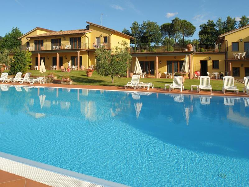 Velký bazén před žlutými rekreačními domy s lehátky a stromy v pozadí.