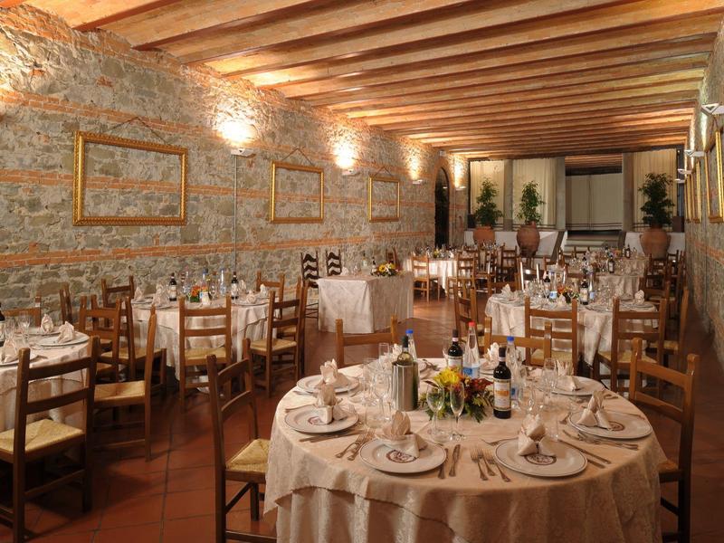 Elegantní restaurace s rustikální kamennou zdí a prostřenými kulatými stoly.