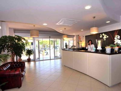 Moderna hall dell'hotel con banco accoglienza, piante e poltrone in pelle.