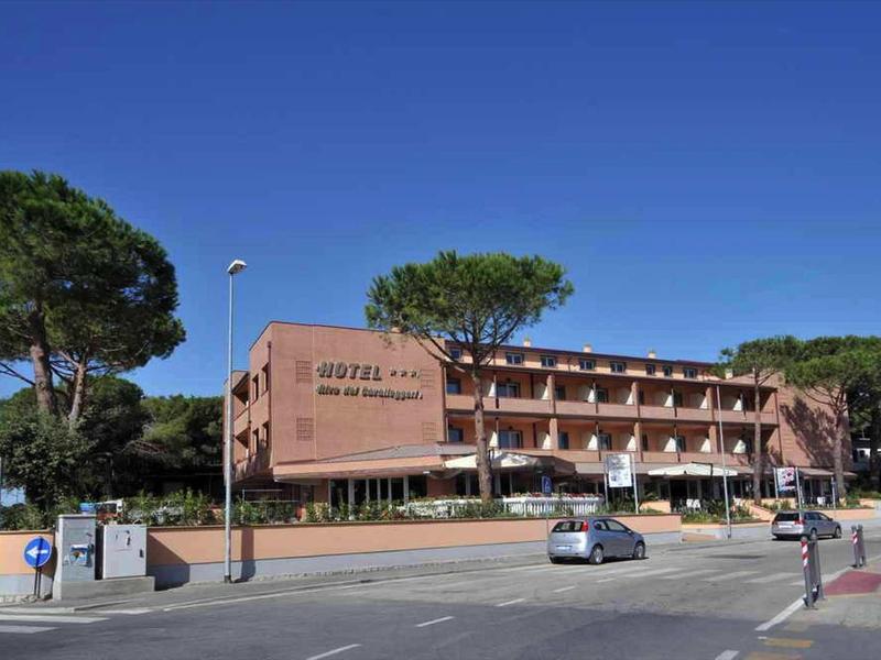 Edificio alberghiero su più piani con alberi e strada tranquilla in primo piano.