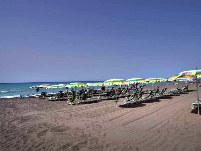 Spiaggia con sabbia scura, file di ombrelloni verdi e lettini vicino al mare