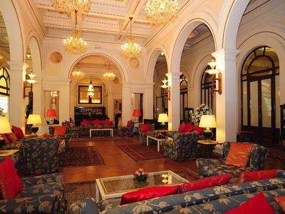 Großer, eleganter Salon mit hohen Bögen, Kronleuchtern und gemütlichen Sofas mit roten Kissen.