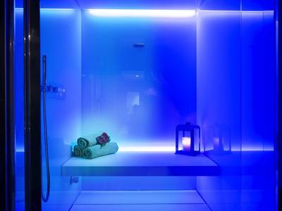 Moderne Dusche mit blauer Beleuchtung, Handtüchern und Kerzenlicht für entspannte Atmosphäre.