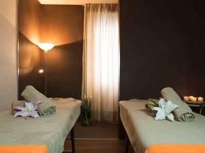 Zwei Massageliegen mit grünen Handtüchern und weißen Blumen in einem warm beleuchteten Raum.