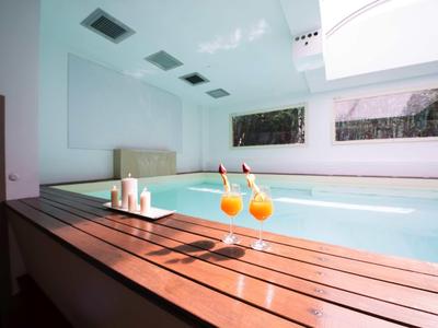 Moderner Wellnessbereich mit großem Innenpool, Holzboden, Kerzen und zwei Orangendrink-Gläsern.