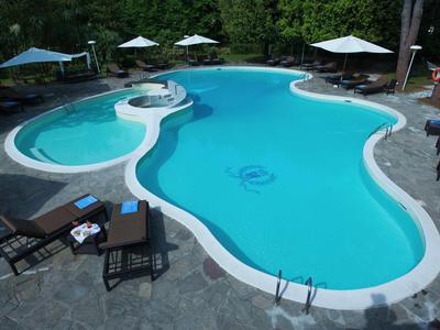 Onregelmatig gevormd zwembad omgeven door ligstoelen en parasols in een hotel tuin.