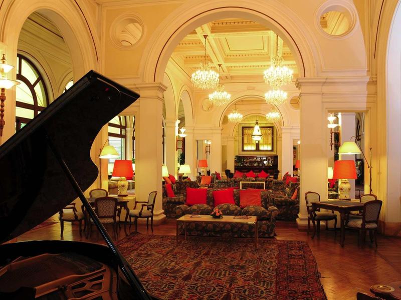 Elegantes Wohnzimmer mit großem Klavier, roten Sofas und warmem Licht in historischem Gebäude.