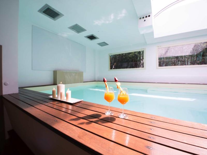 Moderner Wellnessbereich mit großem Innenpool, Holzboden, Kerzen und zwei Orangendrink-Gläsern.