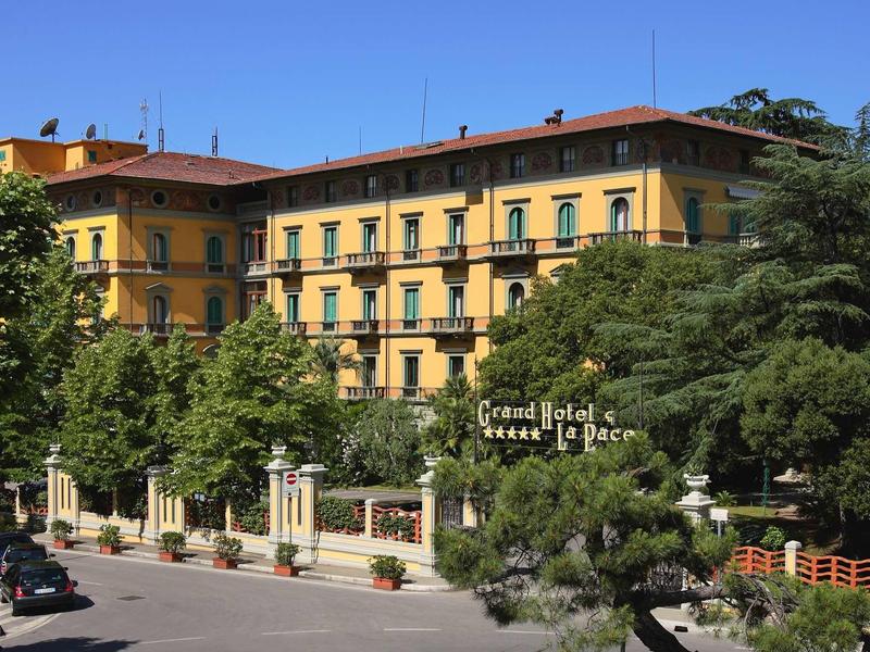Großes gelbes Hotelgebäude mit mehreren Stockwerken, umgeben von grünen Bäumen und blauem Himmel.
