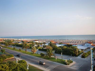 Strada con palme vicino al mare e spiagge con ombrelloni sotto un cielo limpido.