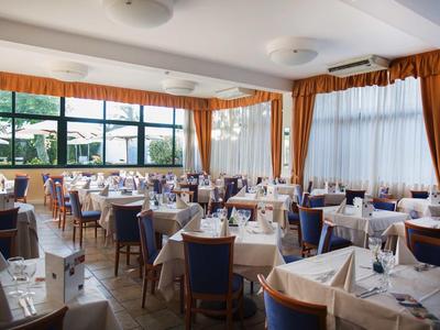 Ristorante luminoso con tavoli apparecchiati, grandi finestre, tende e sedie.
