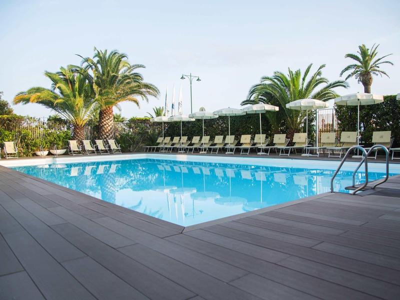 Piscina moderna dell'hotel con lettini e palme in un ambiente soleggiato