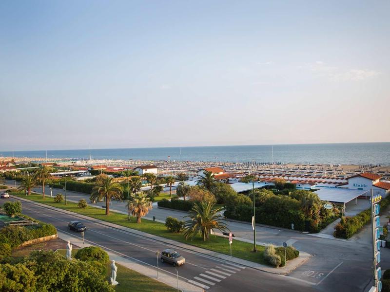 Strada con palme vicino al mare e spiagge con ombrelloni sotto un cielo limpido.