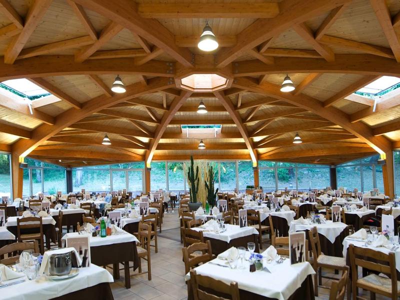 Ampia sala ristorante con soffitto a volte in legno e tavoli apparecchiati con tovaglie bianche.