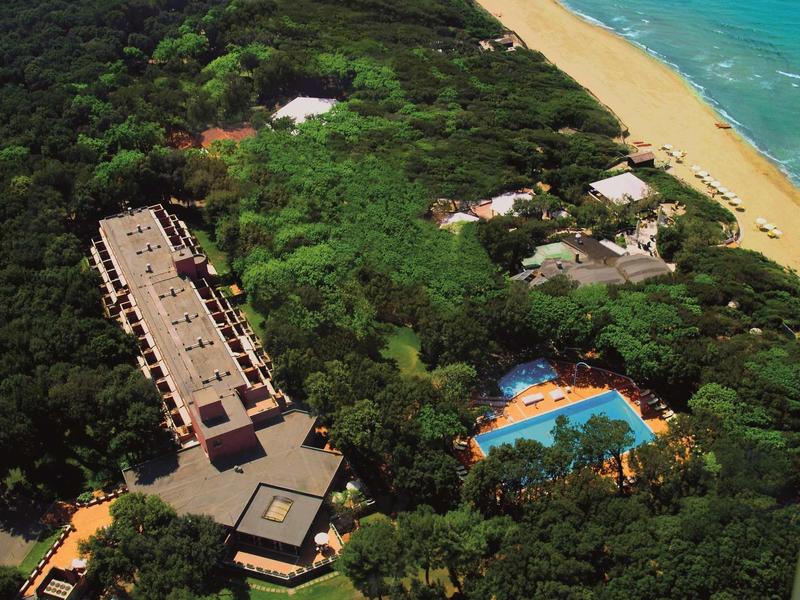 Complesso alberghiero con più edifici, piscina e spiaggia circondati da fitte vegetazione.