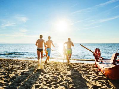 Tre uomini corrono verso il mare sulla spiaggia accanto a una barca di salvataggio al tramonto.