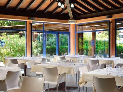 Ristorante luminoso con tavoli, sedie bianche e grandi finestre con vista sul giardino.