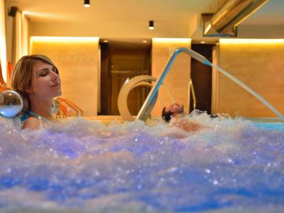 Donna rilassata in una vasca idromassaggio con bolle in un'area benessere illuminata modernamente.