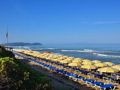 Spiaggia con molti ombrelloni gialli e lettini blu sotto un cielo limpido.