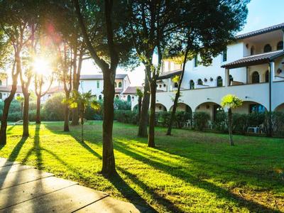 Parco illuminato dal sole con alberi e sentiero lastricato davanti a un edificio dell'hotel.