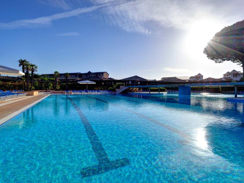 Grande piscina all'aperto con acqua cristallina e lettini sotto ombrelloni al tramonto.