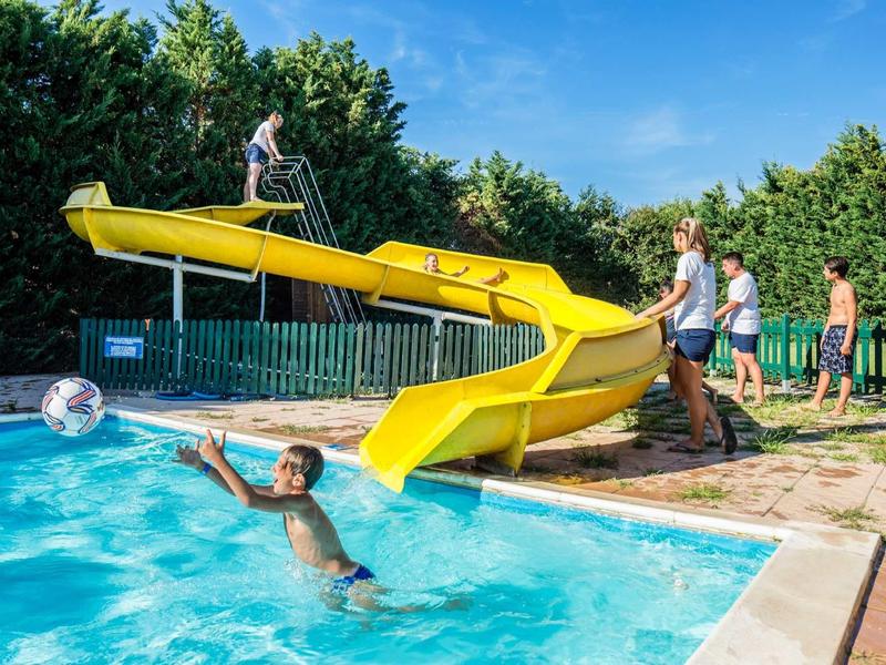 Bambini si divertono nuotando in piscina e sulla scivolo d'acqua in una giornata di sole.