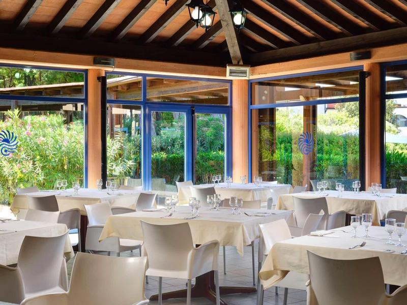 Ristorante luminoso con tavoli, sedie bianche e grandi finestre con vista sul giardino.