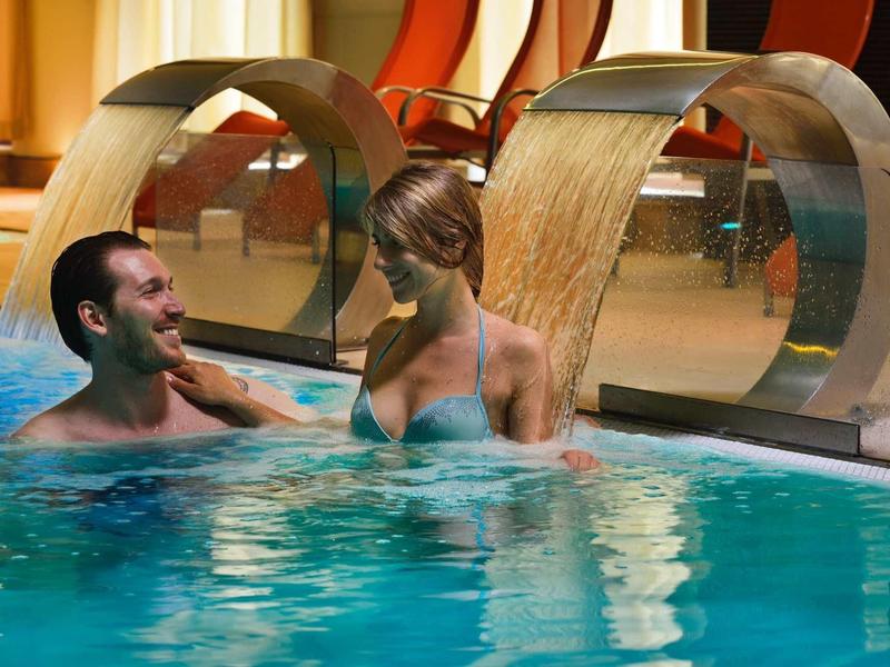 Un uomo e una donna si rilassano in una piscina sotto cascate in una spa dell'hotel.