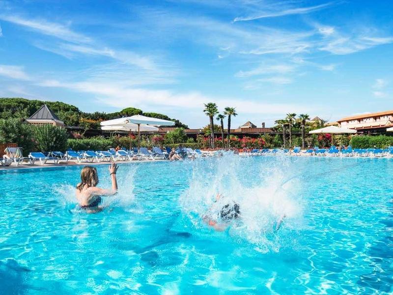 Grande piscina con acqua schizzante e ospiti in un resort alberghiero soleggiato.