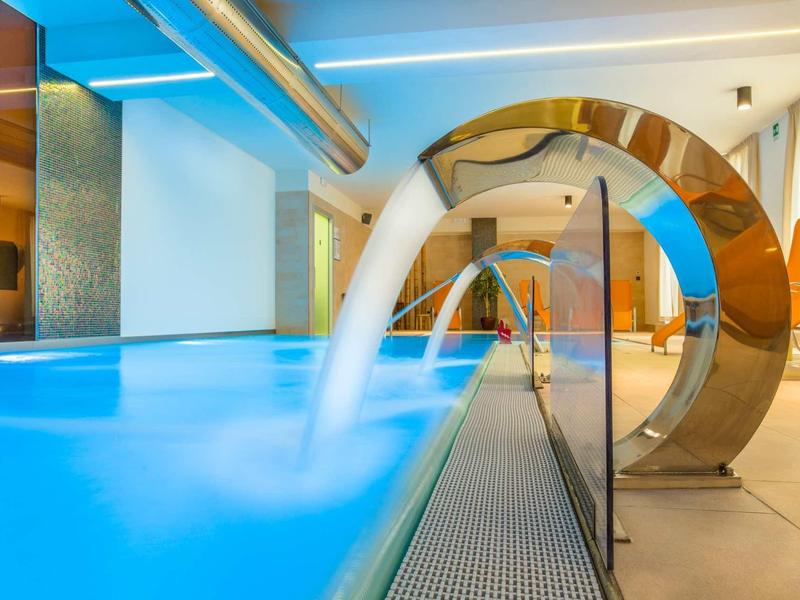 Piscina interna moderna con cascata in acciaio inossidabile curvato nell'area benessere.