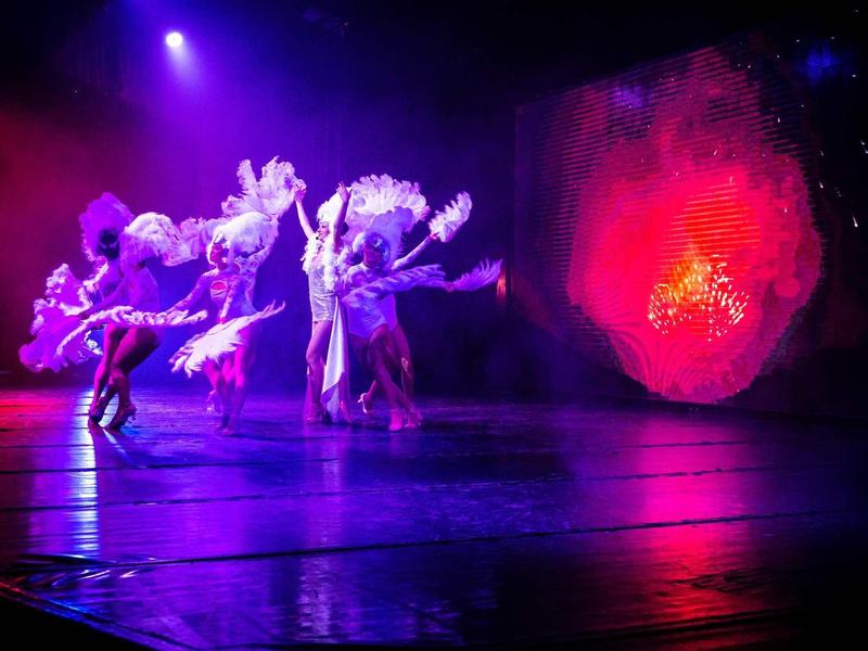 Ballerini in costumi luminosi su un palco illuminato a colori.