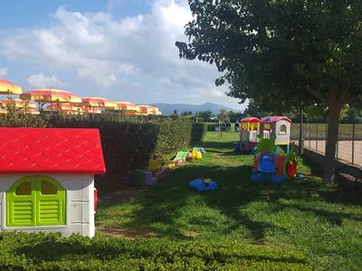 Dětské hřiště s domečkem a herními prvky v zelené hotelové oblasti za slunečného počasí.