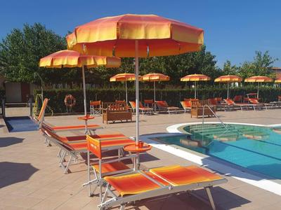 Prostor u bazénu s oranžovými lehátky a slunečníky v slunečný den.