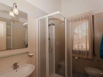 Malá koupelna se sprchovým koutem, umyvadlem, zrcadlem a oknem se záclonou.