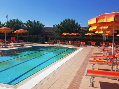 Piscine de loisirs avec chaises longues et parasols orange par une journée ensoleillée.