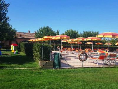 Freizeitpark mit bunten Sonnenschirmen, Sitzbänken und kleinem Spielhaus bei sonnigem Wetter.