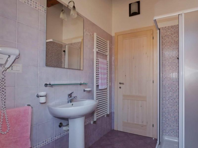 Malá koupelna s umyvadlem, zrcadlem, sprchou a topným žebříkem na ručníky.