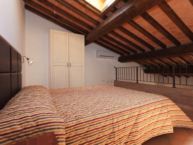 Příjemná ložnice s nízkým stropem z dřevěných trámů a manželskou postelí s pruhovaným povlakem.