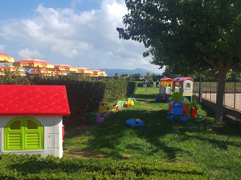 Dětské hřiště s domečkem a herními prvky v zelené hotelové oblasti za slunečného počasí.