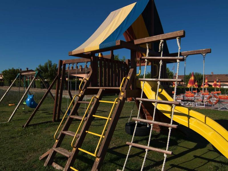 Dětské hřiště se skládacím rámem a žlutou skluzavkou na trávě pod jasnou oblohou