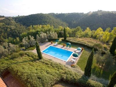 Bazén s lehátky v kopcovité zelené krajině s cypřiši a lesy.